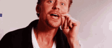 a man with a beard is making a funny face while holding his finger to his face .