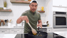 a man is stirring something in a frying pan with a wooden spoon in a kitchen .