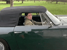 a man is driving a green convertible car with a black top