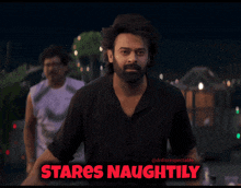 a man in a black shirt stands in front of a sign that says " stares naughtyly "