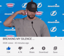 a man wearing a hat stands in front of a microphone with the words breaking my silence below him