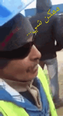 a man wearing sunglasses and a hard hat has arabic writing on his back
