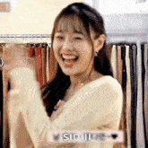 a young woman is laughing in front of a clothes rack .