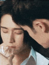 a man is kissing another man 's forehead while holding a glass .