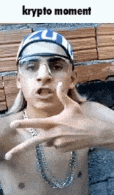 a shirtless man wearing a bandana , glasses , and a chain is making a hand gesture .