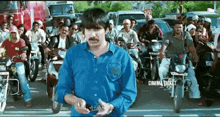 a man in a blue shirt is standing in front of a crowd of people on motorcycles with a cinema ticket advertisement in the background