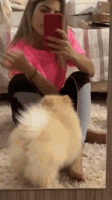 a woman is taking a selfie with her phone while sitting on the floor next to a dog .