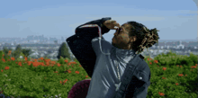 a man with dreadlocks is standing in a field of flowers looking up at the sky
