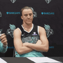 a female basketball player is sitting at a table with her arms crossed in front of a barclays logo