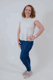 a woman wearing a white shirt and blue jeans is smiling
