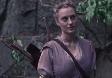 a woman in a purple dress is holding a bow and arrow on her back .