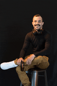 a man wearing headphones and a black shirt sits on a stool