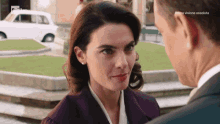 a woman in a purple coat is looking at a man in a suit and the words prima visione absolute are on the bottom