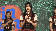 a girl in a plaid dress is holding a microphone while standing in front of a group of girls .