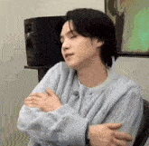 a young man in a sweater is sitting in a chair with his arms crossed .