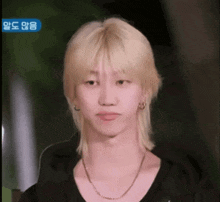 a man with blonde hair is wearing a black shirt and a necklace