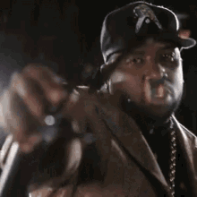 a man wearing a hat and a jacket is holding a microphone and pointing at the camera .