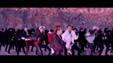 a group of people are dancing in front of a rock wall in a video .