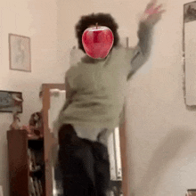 a man is jumping in the air with a red apple in front of his face .