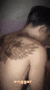 a shirtless man has a tattoo on his back that says enggang