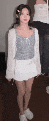 a girl wearing a plaid top and a white skirt stands in front of a mirror