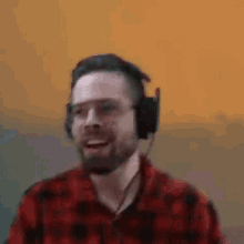 a man with a beard is wearing headphones and a plaid shirt .