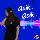 a woman wearing headphones stands in front of a blue background with the words asik asik written in white