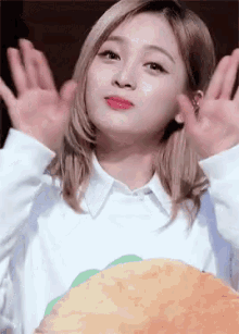 a woman in a white shirt is holding a stuffed animal and waving at the camera .