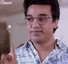 a man wearing glasses and a blue shirt is pointing at something with his finger .