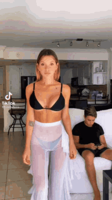 a woman in a bikini is standing next to a man on a couch .