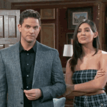 a man in a suit stands next to a woman in a plaid dress