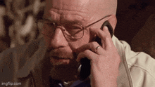 a man with glasses and a beard is talking on a cell phone .
