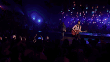 a man singing into a microphone while playing a guitar in front of a crowd