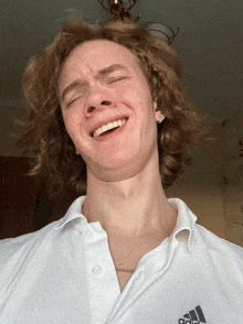 a young man wearing a white adidas shirt is smiling with his eyes closed