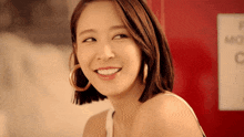 a woman wearing hoop earrings smiles in front of a sign that says mop