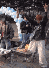 a man wearing a 1987 sweatshirt is standing in front of a barbecue
