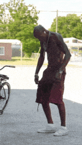 a shirtless man in red shorts and white sneakers is standing in front of a bicycle