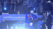 a man wearing a mask stands in front of a sign that says ' baytalhilal '