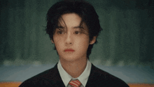 a young man in a suit and tie is looking at the camera with a sad look on his face .