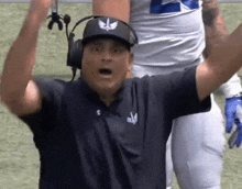 a football coach wearing headphones and a hat with an eagle on it is raising his arms in the air .