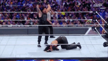 a wrestler is kneeling down in a wrestling ring while another wrestler stands in the corner .