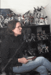 a woman is sitting in front of a microphone in front of a shelf of action figures
