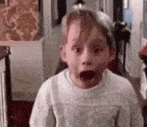 a young boy is making a surprised face while wearing a white sweater .