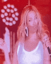 a woman in a white tank top is holding a microphone and making a funny face