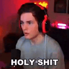 a young man wearing headphones is sitting in front of a microphone and says holy shit .