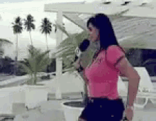 a woman in a pink shirt is holding a microphone and dancing .