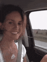 a woman wearing a necklace with the letter s on it is smiling while sitting in a car