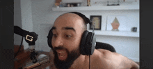 a shirtless man with a beard is wearing headphones and talking into a microphone .
