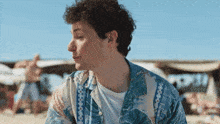 a man with curly hair is wearing a hawaiian shirt on the beach