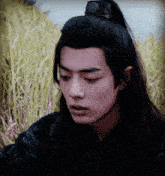 a young man with long black hair is standing in a field